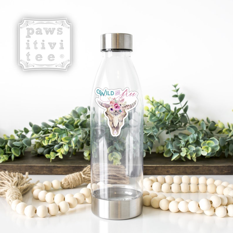 May include: A clear plastic water bottle with a stainless steel lid and base. The bottle has a sticker on it that says "Wild and Free" with a floral skull design.