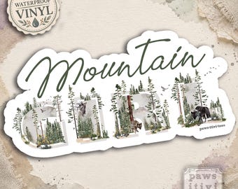Pode incluir: Um adesivo de vinil à prova d'água com o texto Mountain GIRL em uma fonte cursiva verde-escura. As letras são preenchidas com uma ilustração de paisagem florestal contendo pinheiros, um cervo, um urso e pássaros. O texto paws-itiv-tees é visível.