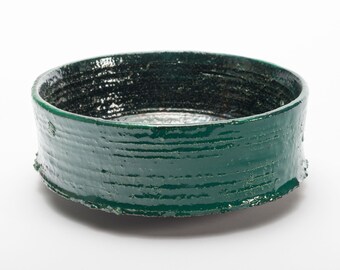 May include: A deep green ceramic bowl with a textured, slightly uneven surface. The bowl has a rounded shape and a wide rim.