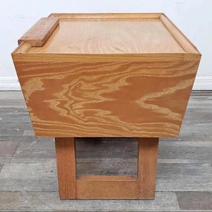 May include: A wooden side table with a rectangular top and a square base. The table is made of light-colored wood with a visible wood grain pattern. The base has an open rectangular design.
