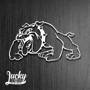 May include: A white silhouette of a bulldog with a snarling expression. The bulldog is lying down with its head turned to the left. The image is on a dark wood background.