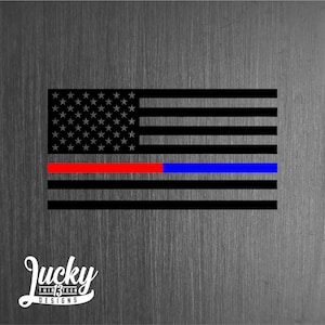 May include: A black and white American flag with a thin red stripe and a thin blue stripe across the middle. The flag is on a textured gray background.