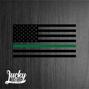May include: A black and white American flag with a thin green stripe across the middle. The flag is on a textured background.