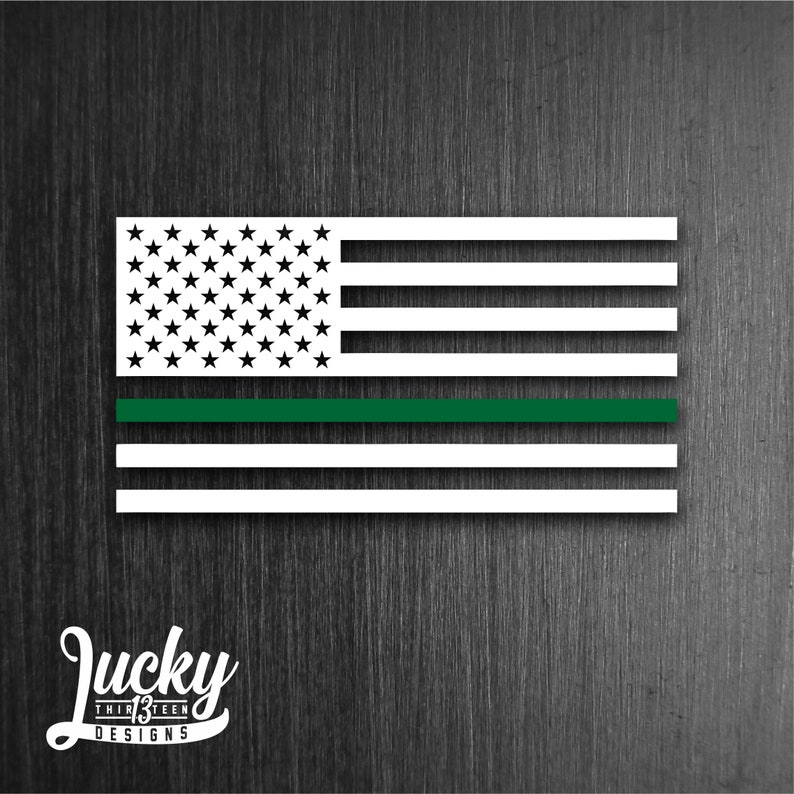 May include: A white American flag with a thin green stripe across the middle. The flag is on a dark wood background. The text "Lucky Thirteen Designs" is below the flag.