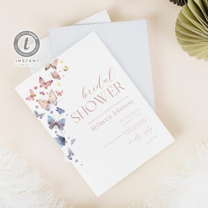 Op de afbeelding: Een witte bruidsdouche-uitnodiging met een roze en blauwe aquarel-vlinderontwerp. De uitnodiging luidt "bridal shower" in roze schrift en bevat de naam van de bruid, datum, tijd en locatie. De tekst "kindly reply by April 30th" staat onderaan de uitnodiging.