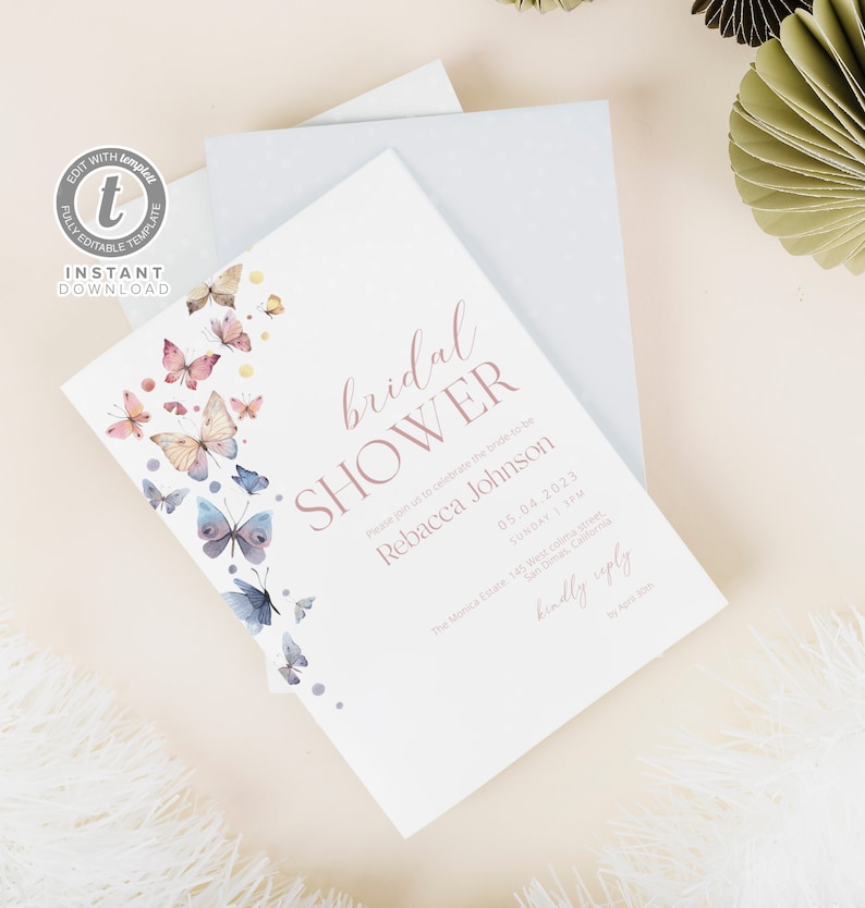 Op de afbeelding: Een witte bruidsdouche-uitnodiging met een roze en blauwe aquarel-vlinderontwerp. De uitnodiging luidt "bridal shower" in roze schrift en bevat de naam van de bruid, datum, tijd en locatie. De tekst "kindly reply by April 30th" staat onderaan de uitnodiging.