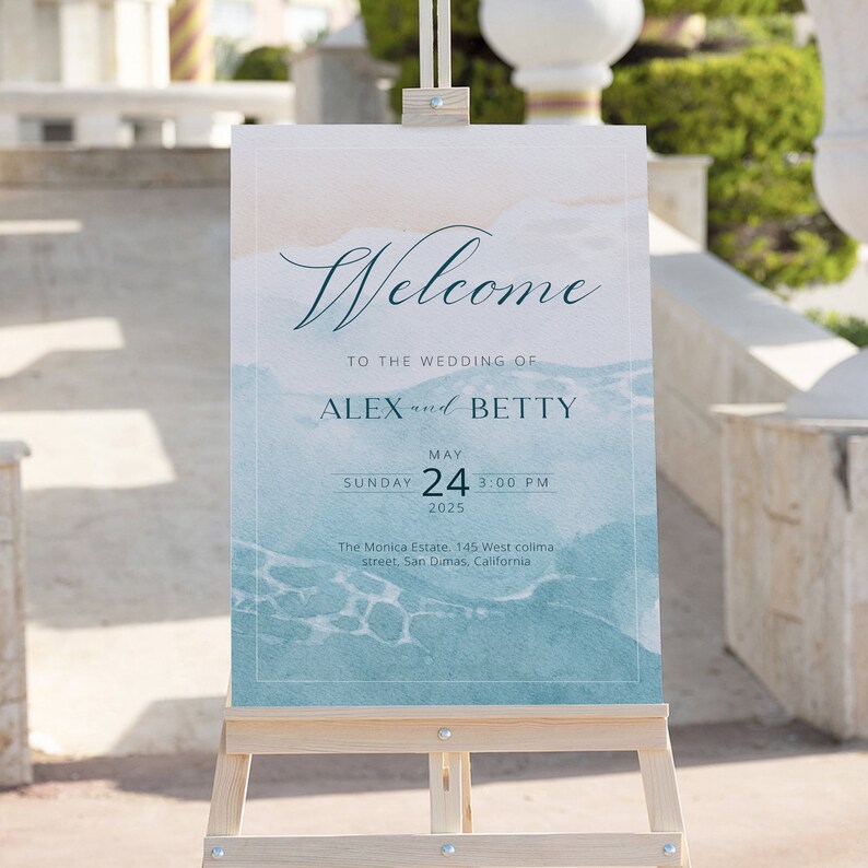 以下が含まれることがあります： 青い水彩画の背景に「AlexとBettyの結婚式へようこそ」という文字が書かれた、結婚式用のウェルカムサイン。サインは木製イーゼルに置かれています。