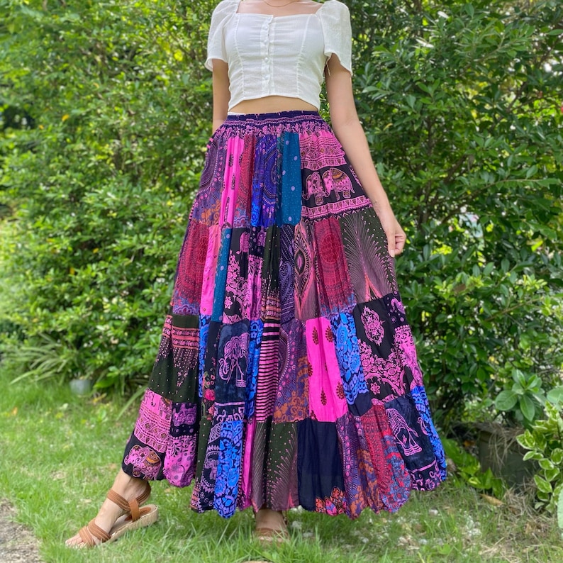 Puede incluir: Una falda larga de patchwork en colores vibrantes, incluyendo rosa, azul y morado. La falda presenta varios patrones y dise&ntilde;os, incluyendo elefantes y motivos de cachemira. La falda se lleva con una camiseta blanca de manga corta. La falda mide unos 90 cm.
