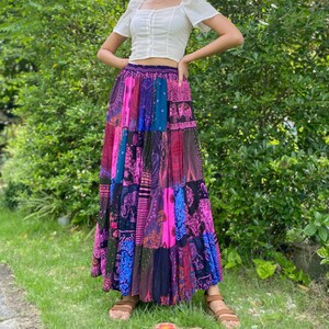 Puede incluir: Una falda larga de patchwork con una vibrante mezcla de colores, incluyendo rosa, azul y negro. La falda tiene una cintura el&aacute;stica y varios paneles de tela estampada. La falda se usa con una blusa blanca de manga corta.