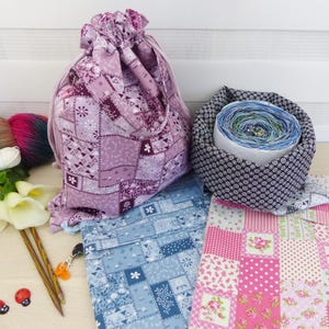 Könnte beinhalten: Eine Sammlung von Stoffbeuteln mit Kordelzug in Patchwork-Mustern in Lila-, Blau- und Rosatönen, neben einer schwarz-weiß gemusterten Garnschale mit einem mehrfarbigen Garnknäuel, Stricknadeln und zwei Marienkäfer-Anhängern.