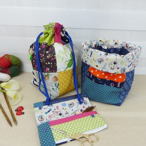 Könnte beinhalten: Drei Patchwork-Stofftaschen zum Verstauen von Garn und Stricknadeln. Die Taschen sind blau, grün, orange und weiß mit verschiedenen Mustern. Die größte Tasche ist eine Kordeltasche mit einer blauen Kordel. Die mittlere Tasche ist eine zylindrische Tasche mit einem blau-weißen Punkte-Muster. Die kleinste Tasche ist eine flache Tasche mit einem Reißverschluss. Die Tasche enthält eine goldene Schere und Stricknadeln.