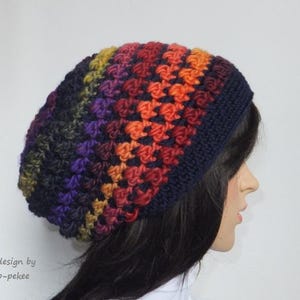 May include: A colourful crocheted beanie hat with a gradient of orange, red, purple, and green. The hat is made with a textured stitch and has a dark blue base.