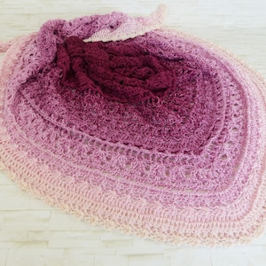 May include: A crocheted shawl with a gradient of pink, purple, and white colors. The shawl is made with a delicate stitch pattern and has a scalloped edge.