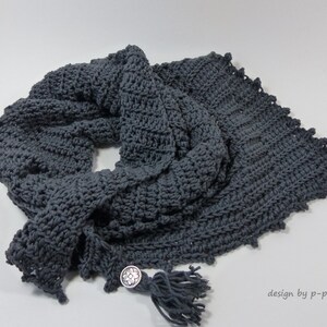 May include: A gray crocheted scarf with a tassel and a silver button. The scarf is folded in half and the tassel is hanging down. The button is on the side of the scarf. "design by p-pekee" is written in the bottom right corner of the image.