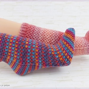 Puede incluir: Dos pares de calcetines de crochet coloridos en una variedad de tonos de rosa, naranja, azul y morado. Los calcetines están hechos con un punto texturizado y se muestran en las piernas de una persona.