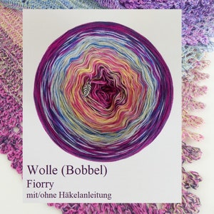 Könnte beinhalten: Ein lebendiger Knäuel Fiorry-Garn in Lila, Rosa, Gelb und Blau, mit einem silbernen Blattanhänger. Das Bild zeigt auch einen gehäkelten Schal in passenden Farben. Der Text auf dem Bild lautet "Wolle (Bobbel) Fiorry mit/ohne Häkelanleitung."