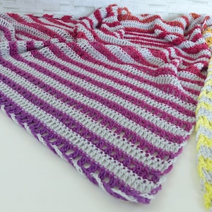 May include: A selection of colourful, handmade crochet shawls. The shawls have a striped pattern in shades of purple, pink, red, yellow, and grey. The crochet work is detailed and the shawls are displayed on a white surface.