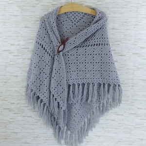 May include: A gray crocheted shawl with fringe, featuring a delicate openwork pattern and a wooden button closure.