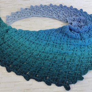 Peut inclure: Un châle crocheté dans un dégradé de couleurs bleu et vert. Le châle est réalisé avec un motif de point délicat et a un bord festonné.