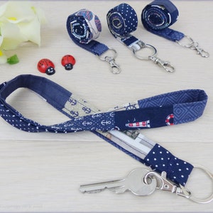 Könnte beinhalten: Ein blaues und weißes gemustertes Lanyard mit einem silbernen Schlüsselring und einem silbernen Schlüssel. Das Lanyard hat ein nautisches Thema mit Ankern und einem Leuchtturm.