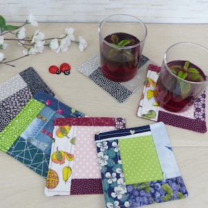 Könnte beinhalten: Sechs bunte Stoffuntersetzer mit verschiedenen Mustern, darunter Früchte, Blumen und geometrische Designs. Die Untersetzer sind aus Patchwork-Stoff gefertigt und haben eine quadratische Form.