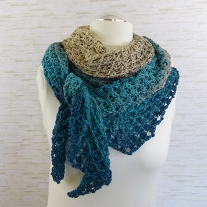 May include: A crocheted shawl with a gradient of blue and green colours. The shawl is made with a delicate openwork stitch and has a beige trim.