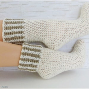 Puede incluir: Un par de calcetines tejidos a crochet con una base blanca y rayas marrones en la parte superior. Los calcetines están hechos con un patrón de punto de waffle.