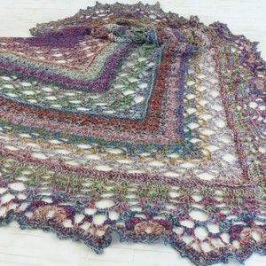 May include: A handmade, multi-colored crochet shawl. The shawl features a variety of colors, including purple, blue, green, and red, creating a gradient effect. The openwork design adds a delicate touch. The edges are scalloped, adding a decorative finish to this wearable accessory.