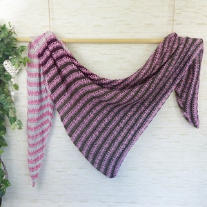 Könnte beinhalten: Ein gestrickter Schal in Rosa und Grau mit Streifen und dreieckiger Form. Der Schal hängt an einer Holzstange.