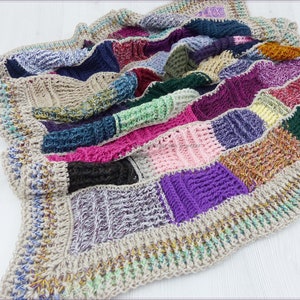 Op de afbeelding: Een veelkleurig gehaakt deken met een beige rand. Het deken is gemaakt van verschillende gekleurde vierkanten, waaronder roze, paars, groen, blauw en bruin.