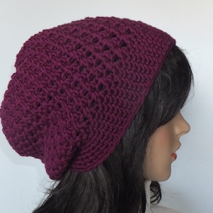 May include: A burgundy crocheted beanie hat with a lacy pattern. The hat is worn on a person with long dark hair.