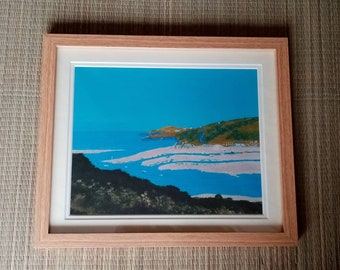 May include: Framed print of a coastal landscape painting. The painting depicts a blue sky, a sandy beach, a body of water, and a green hill in the distance.