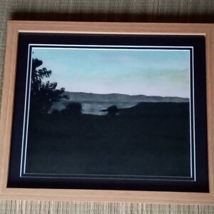 May include: A framed black and white landscape photograph of a silhouetted forest with a lake in the distance. The sky is a light blue with a hint of pink in the horizon.