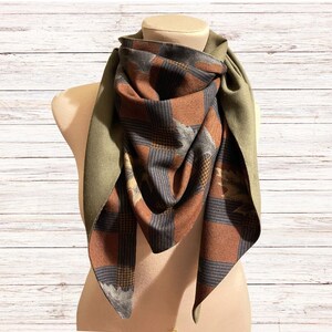 May include: A reversible scarf with a brown and blue plaid pattern on one side and a solid olive green on the other side.