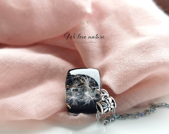 May include: A rectangular pendant necklace with a black background, featuring white dandelion seeds encased in resin. The pendant is attached to a silver chain with a decorative floral charm. The text "We love nature" is visible.