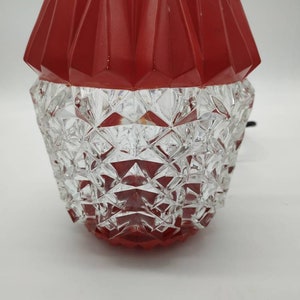 Puede incluir: Una l&aacute;mpara colgante vintage con una pantalla roja facetada y una base de vidrio transparente con dise&ntilde;o de diamantes. La l&aacute;mpara tiene una parte superior negra y un interior rojo, creando un contraste llamativo. Esta l&aacute;mpara retro es un art&iacute;culo de decoraci&oacute;n &uacute;nico.