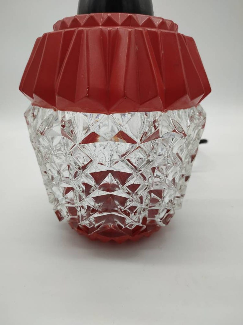 Puede incluir: Una l&aacute;mpara colgante vintage con una pantalla roja facetada y una base de vidrio transparente con dise&ntilde;o de diamantes. La l&aacute;mpara tiene una parte superior negra y un interior rojo, creando un contraste llamativo. Esta l&aacute;mpara retro es un art&iacute;culo de decoraci&oacute;n &uacute;nico.