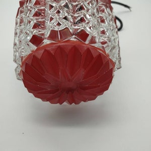 Puede incluir: Una l&aacute;mpara vintage de cristal rojo y transparente. La l&aacute;mpara tiene un patr&oacute;n geom&eacute;trico en el cristal transparente y una base roja facetada. Un cable negro se extiende desde la parte superior.