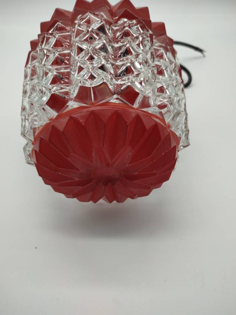 Puede incluir: Una l&aacute;mpara vintage de cristal rojo y transparente. La l&aacute;mpara tiene un patr&oacute;n geom&eacute;trico en el cristal transparente y una base roja facetada. Un cable negro se extiende desde la parte superior.