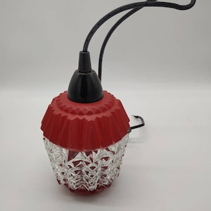 Puede incluir: Una l&aacute;mpara colgante vintage con una pantalla roja acanalada y una base de vidrio transparente facetado. La l&aacute;mpara tiene un cable negro y una parte superior negra. La l&aacute;mpara est&aacute; dise&ntilde;ada para colgar del techo.