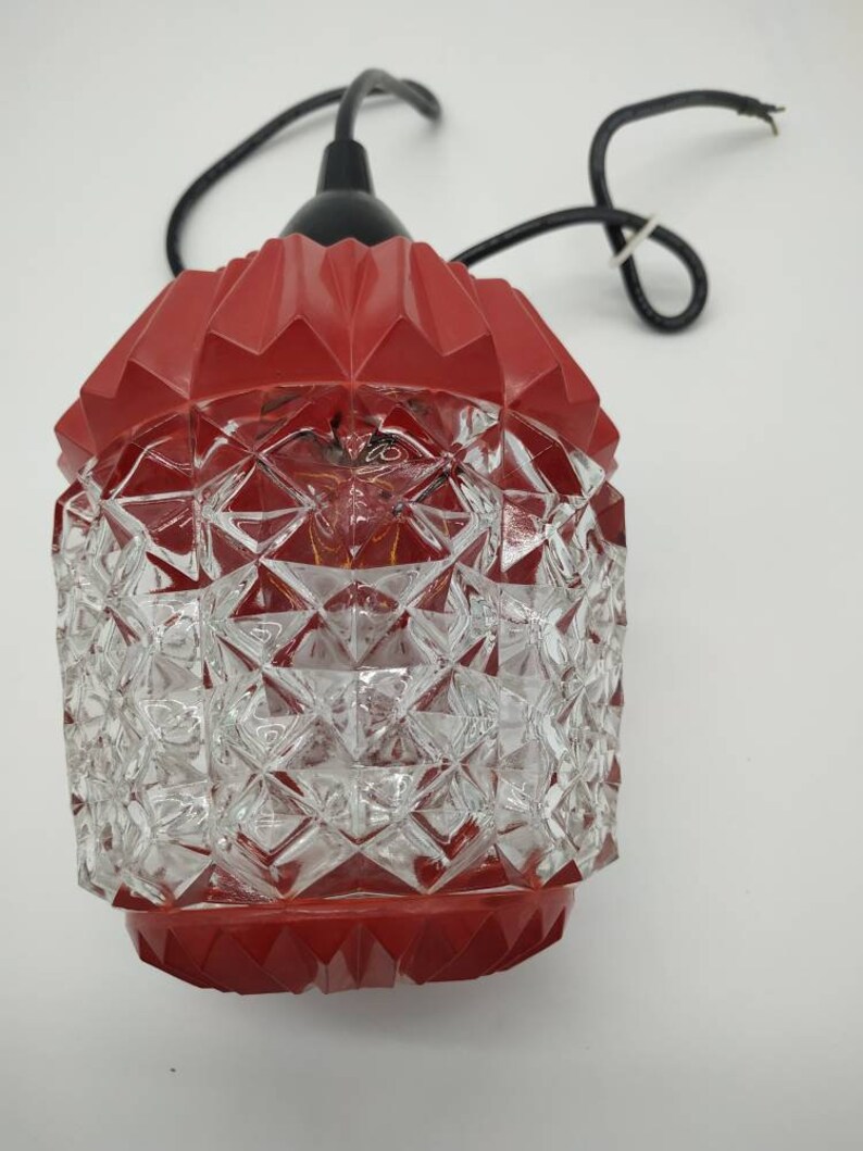 Puede incluir: L&aacute;mpara colgante vintage con una parte superior roja geom&eacute;trica y una pantalla de cristal transparente con dise&ntilde;o de diamantes. La l&aacute;mpara tiene un cable negro y est&aacute; dise&ntilde;ada para colgar. Dise&ntilde;o retro y decorativo.