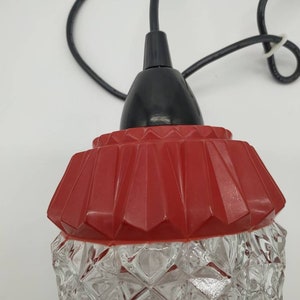 Puede incluir: Una l&aacute;mpara colgante vintage con una pantalla de vidrio transparente con dise&ntilde;o de diamantes y una parte superior roja geom&eacute;trica. La l&aacute;mpara tiene un cable negro y una tapa negra. La luz est&aacute; dise&ntilde;ada para colgar del techo.
