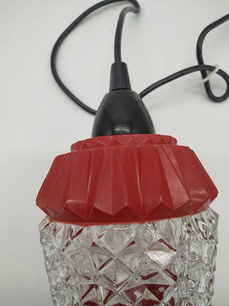 Puede incluir: Una l&aacute;mpara colgante vintage con una pantalla de vidrio transparente con dise&ntilde;o de diamantes y una parte superior roja geom&eacute;trica. La l&aacute;mpara tiene un cable negro y una tapa negra. La luz est&aacute; dise&ntilde;ada para colgar del techo.