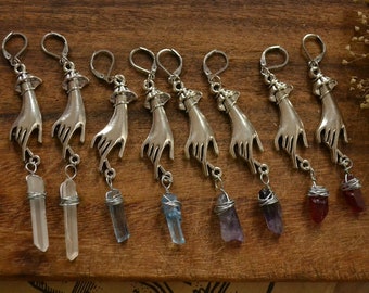 Puede incluir: Siete pares de pendientes colgantes de plata con detalles de cristal. Cada pendiente presenta un dije de mano de plata con un colgante de cristal que cuelga de él. Los cristales son transparentes, azules, morados y rojos.