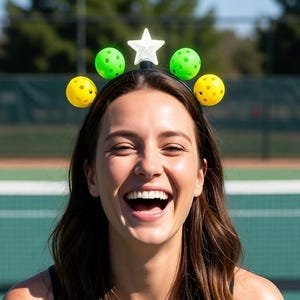 May include: A black headband featuring a central white star ornament flanked by two bright green pickleballs and two yellow pickleballs, arranged symmetrically along the top of the band to create a decorative accessory for sports enthusiasts.