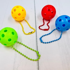 May include: Four colourful keychains with hollow plastic balls in yellow, red, blue, and green. Each ball has a chain attached to it.