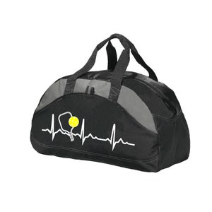 May include: A black and grey duffel bag featuring a white heartbeat line graphic that incorporates a pickleball paddle and a yellow pickleball. The bag has two black top handles and a zippered main compartment with a structured, rounded shape.