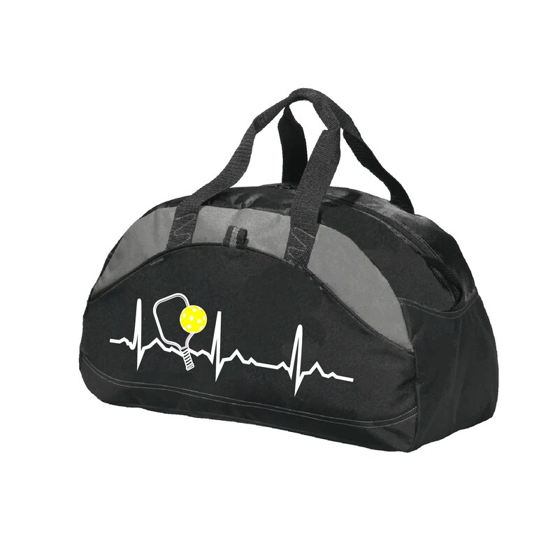 May include: A black and grey duffel bag featuring a white heartbeat line graphic that incorporates a pickleball paddle and a yellow pickleball. The bag has two black top handles and a zippered main compartment with a structured, rounded shape.
