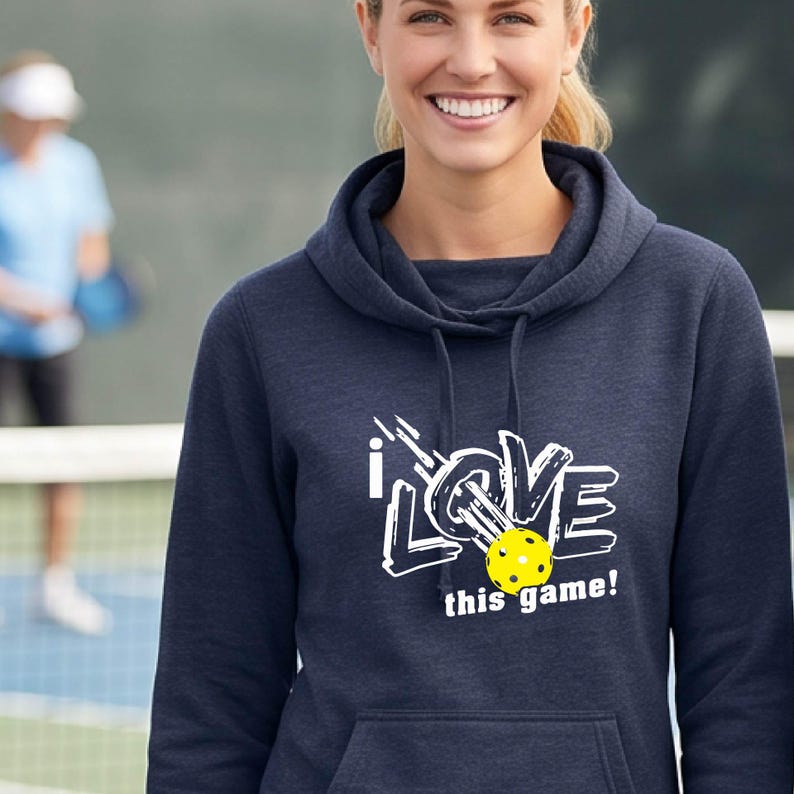 A navy blue hooded sweatshirt featuring a white graphic print that reads "i LOVE this game!" with a bright yellow pickleball replacing the letter "O" in the word "LOVE". The hoodie includes a front kangaroo pocket and drawstrings.