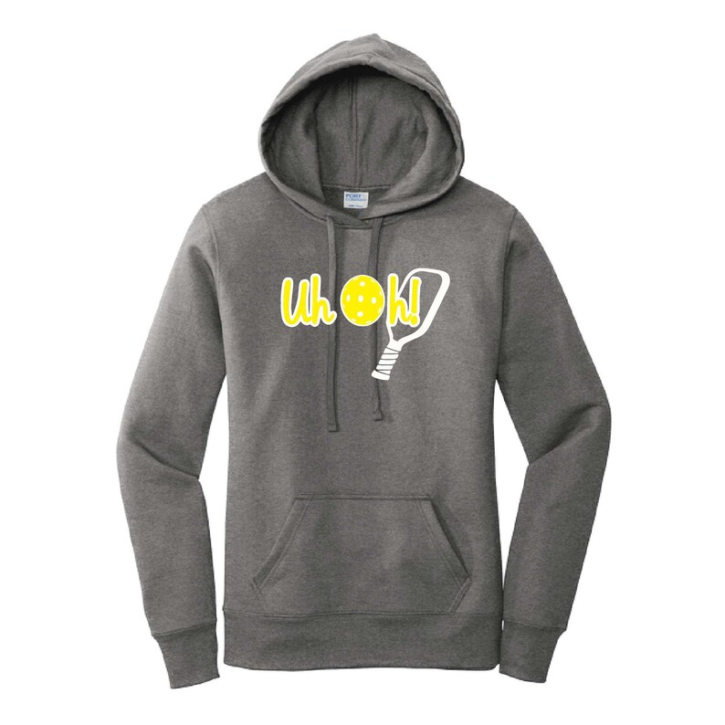 Op de afbeelding: Een donkergrijze hoodie met een voorzak en een trekkoord. De hoodie heeft de tekst "Uh Oh!" in het geel, samen met een gele pickleball en een witte pickleball paddle graphic. De hoodie is gemaakt van een zacht materiaal.
